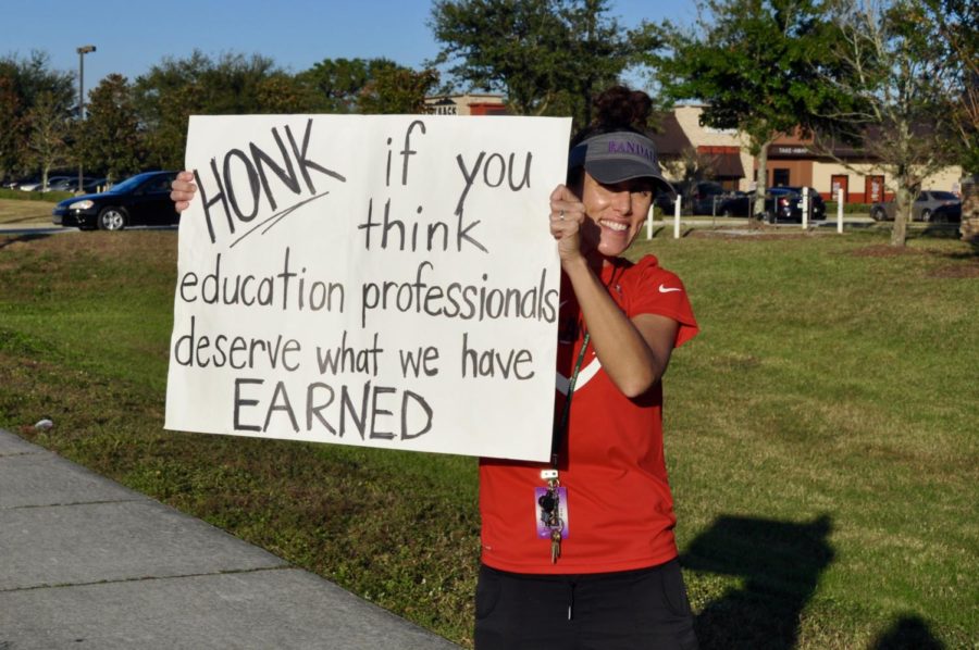 Teacher protests budget cuts that revoke promised pay raises outside Randall Middle School.